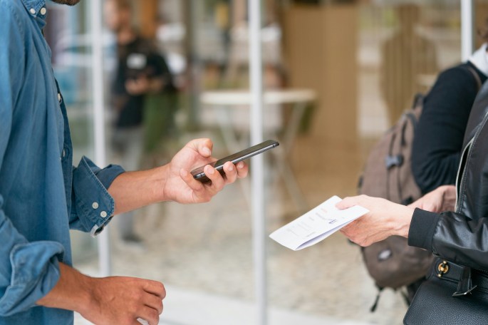 One person holding a piece of paper and another person holding their phone out to scan something on the paper